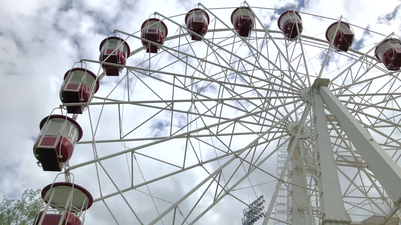 вид на вращающееся колесо обозрения с красными каютами на облачном небе