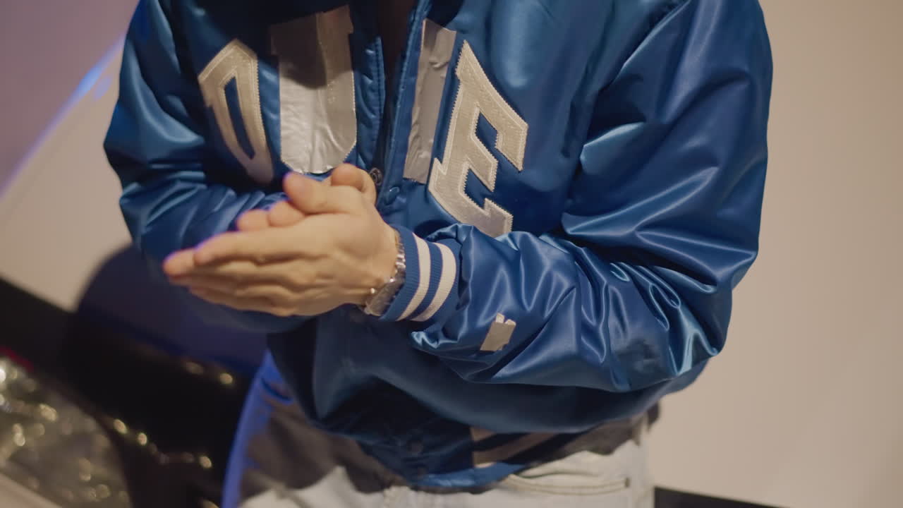 밤길에 차에 기대어 서서, 셔츠 커프스를 만지며 곰곰이 생각하는 듯 먼 헤드라이트를 응시하는 남자의 모습이 데님과 야구 점퍼 차림으로 포착되었어요.