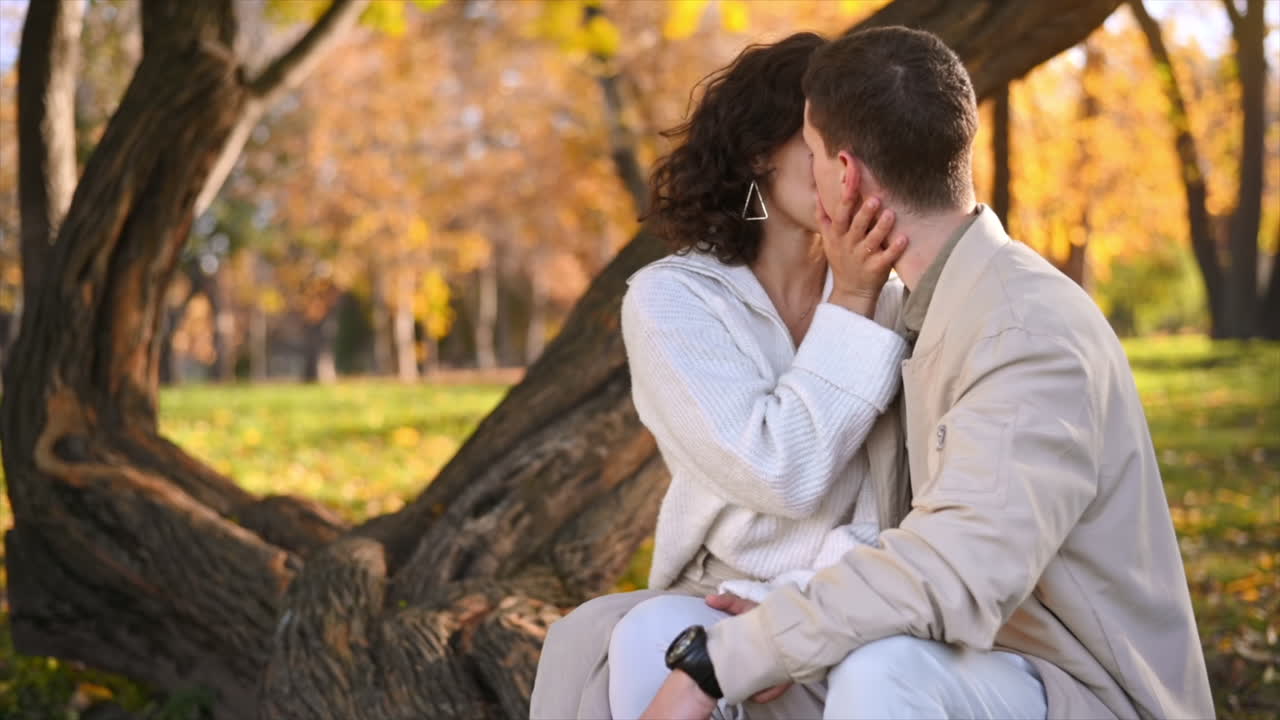 Una coppia romantica in un parco autunnale. Si baciano. Atmosfera autunnale, alberi ingialliti e foglie tutt'intorno. Rallentatore