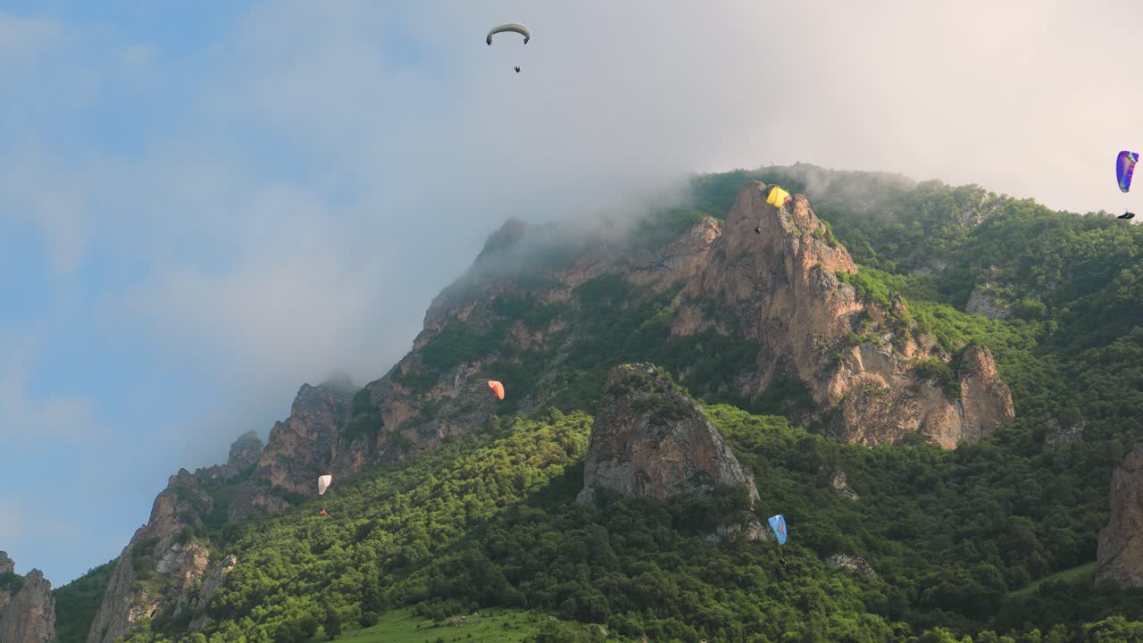 패러글라이딩 조종사들은 구름과 푸른 산들 사이에서 패러글라이더를 비행합니다.