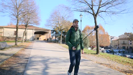 tourist walks on sidewalk in city park filming with action camera on selfie stick