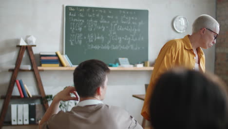 female teacher walking in classroom and helping students on lesson