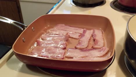 uncured bacon cooking in a square pan on an electric stove