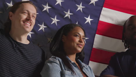 retrato de estudio de un grupo multicultural de amigos con la bandera estadounidense detrás de ellos celebrando el 4 de julio, día de la independencia.