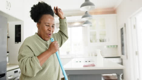 Feliz-Mujer-Mayor-Afroamericana-Bailando-Y-Cantando-En-Una-Cocina-Soleada,-Cámara-Lenta