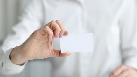 female hand holds out business card at workplace closeup