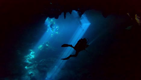 silhouette of a diver in a cave with light beams in the background