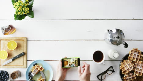 Top-view-man-browsing-vacation-photographs-using-smartphone-at-breakfast-Belgian-waffles-and-coffee-hands-from-above---Red-Epic-Dragon