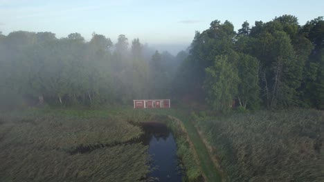 Cabaña-De-Lago-Sueco-Rojo-En-Bosque-Brumoso,-Tiro-De-Retroceso-De-Drones