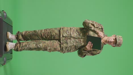 cuerpo lleno de hombre asiático soldado tomando nota en una tableta mientras caminaba en el estudio de fondo de la pantalla verde