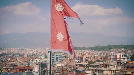 the national flag of nepal waving in the wind against the bright blue sky and the kathmandu city view. -tilt down shot