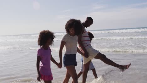 Padres-Afroamericanos-Sonrientes-Y-Sus-Hijos-Caminando-Y-Tomados-De-La-Mano-En-La-Playa.