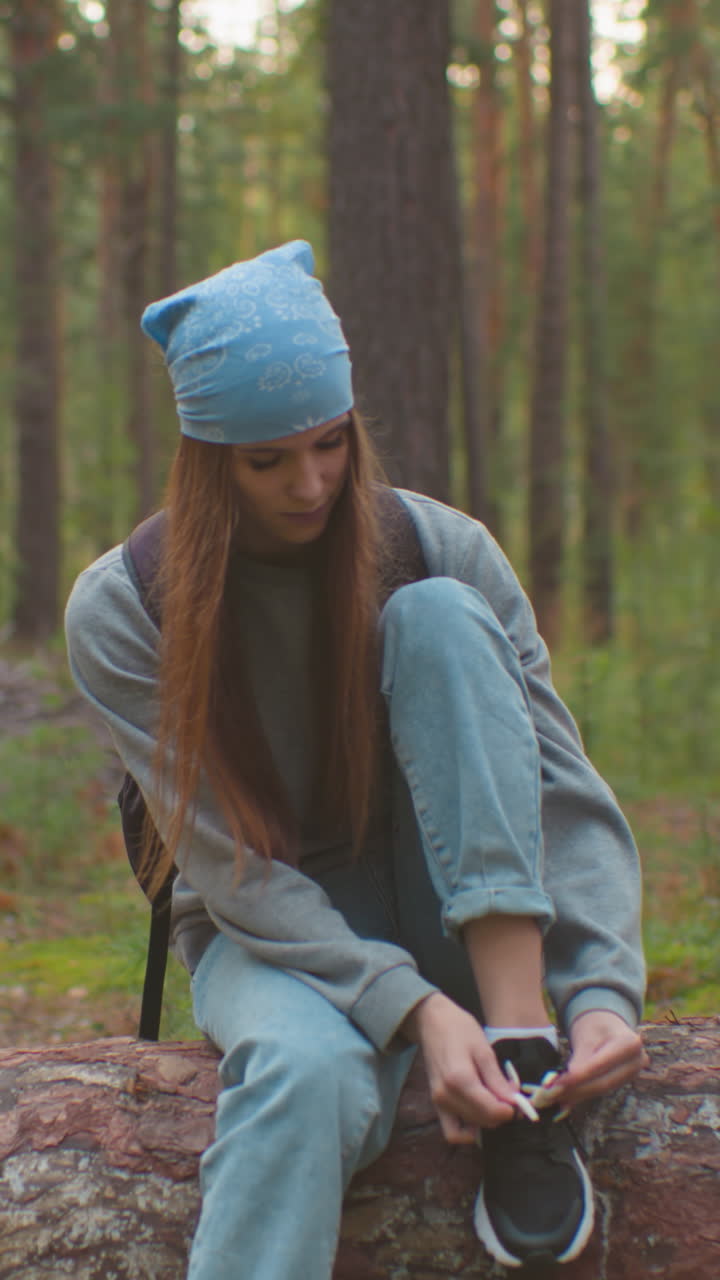 amigos toman un descanso en un bosque, una sentada en un árbol caído atando su zapato, mientras que su compañera está cerca con una mochila roja, participando en una conversación, árboles altos y vegetación los rodean