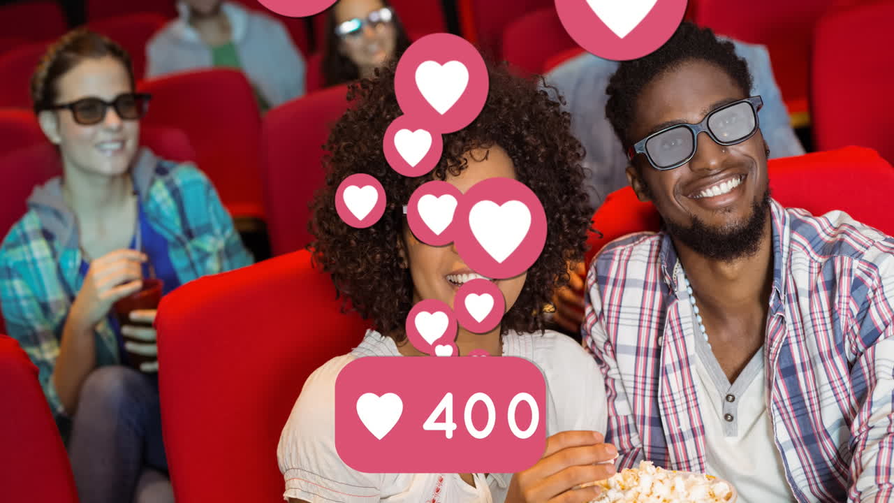 Animação de ícones de coração sobre casal afro-americano sorrindo comendo pipoca no cinema