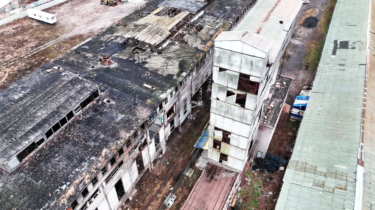 Empty boxes of an old plant buildings. Damaged roofs and walls of industrial architecture. Premises still in use at the backdrop.