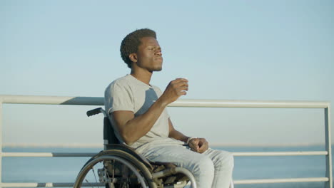 young man in wheelchair enjoying takeaway coffee at seafront