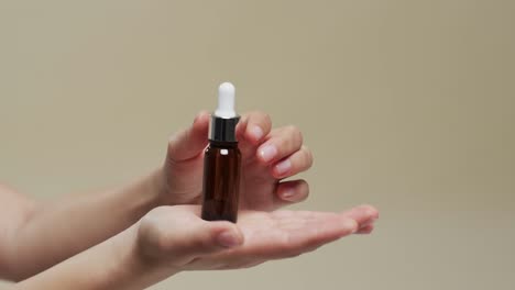 hands of woman holding flask with cosmetic on beige background with copy space, slow motion