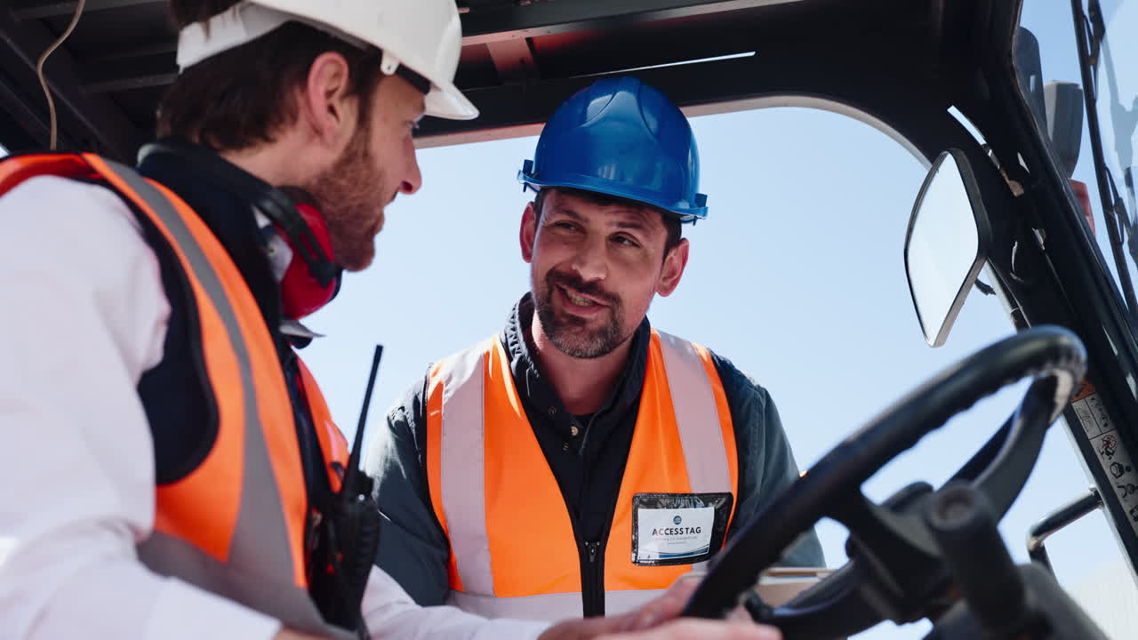 Two Industrial Workers in Hard Hats Discussing Plans in a Forklift
