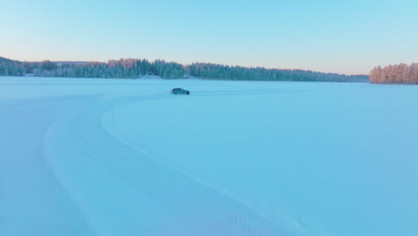 aerial view following drifting car speeding on norbotten woodland ice lake at sunrise