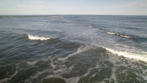 disparo aéreo de avión no tripulado en la playa moviéndose a lo largo de las rocas hacia el muelle y la torre de la casa de luz marcando el canal del barco