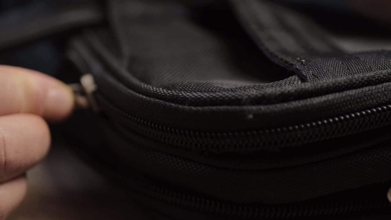 Hand pulling metal zip  to open black briefcase
