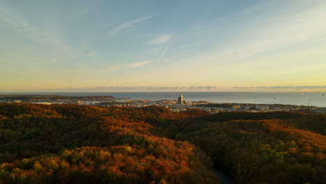 Landschaft-Des-Herbstwaldes-Mit-Laubbäumen-Und-Roten-Und-Orangefarbenen-Baumkronen-An-Der-Grenze-Der-Stadt-Gdynia-Bei-Sonnenuntergang,-Luftdrohne-Fliegt-Auf