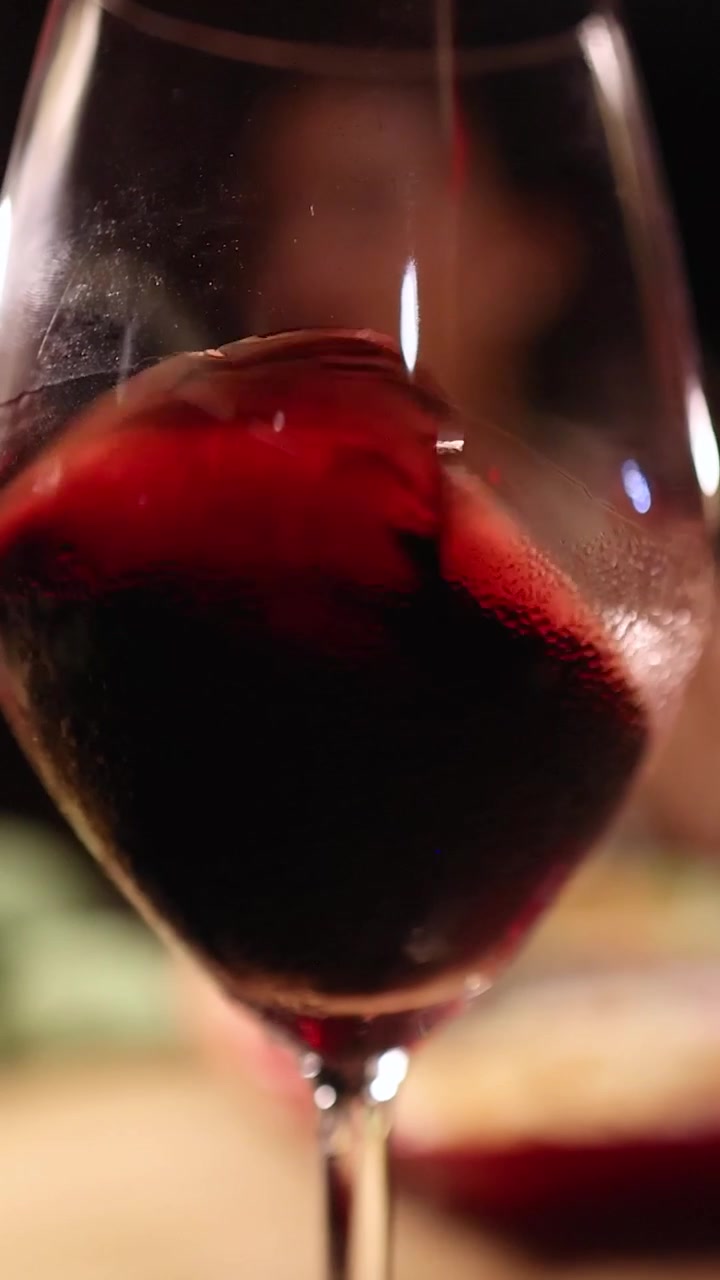 Un primo piano verticale di vino rosso che volteggia all'interno di un bicchiere con un'illuminazione bokeh calda.