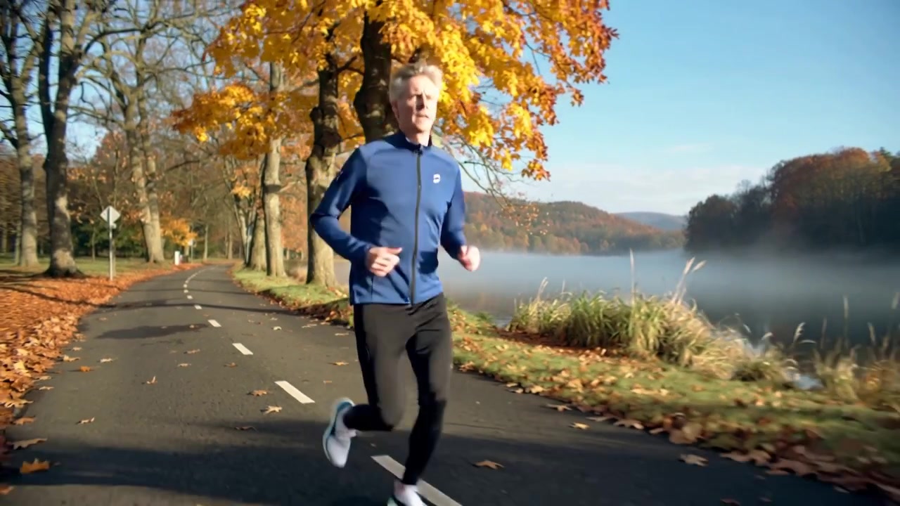 Jogger uomo che corre e si allena all'alba, avvicinandosi alla telecamera lungo il sentiero del lago, con una giacca blu.