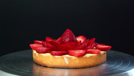 el pastelero está colocando la última fresa encima de una tarta rellena de crema pastelera