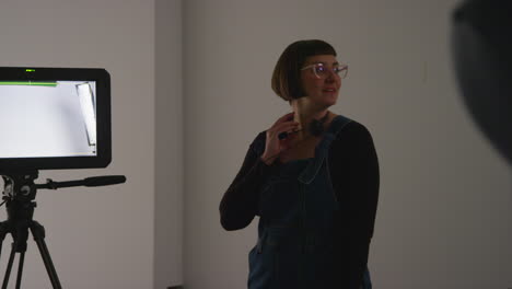 female film production assistant with headset standing by monitor on movie or video shoot in studio