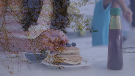 autumn tree branches overlaying pancakes with blueberries and syrup bottle on table