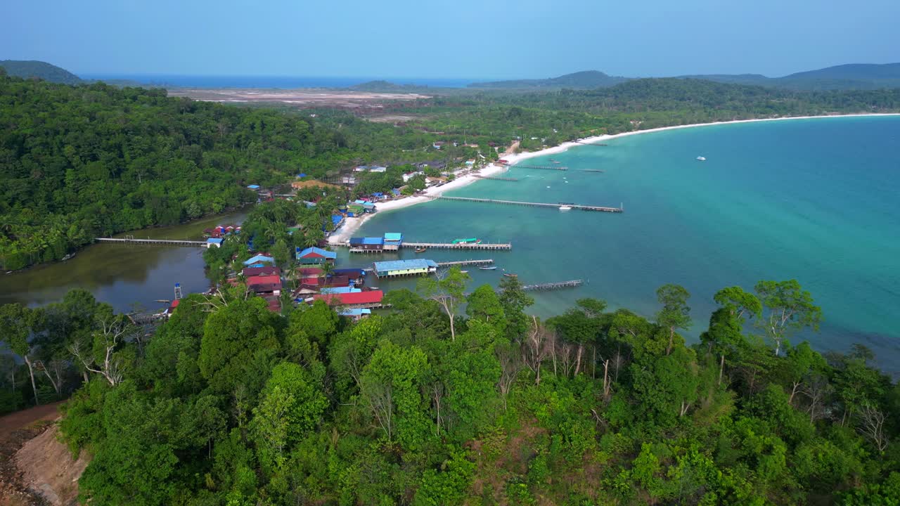 Koh Rong island, Cambodia, showcasing a fishing village with traditional houses on stilts, turquoise water, and lush vegetation. Unbelievable aerial view flight static tripod hovering drone