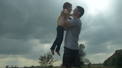 a happy, loving father holding and hugging his son for a warm, positive family moment outside under the sunlight shines through clouds.