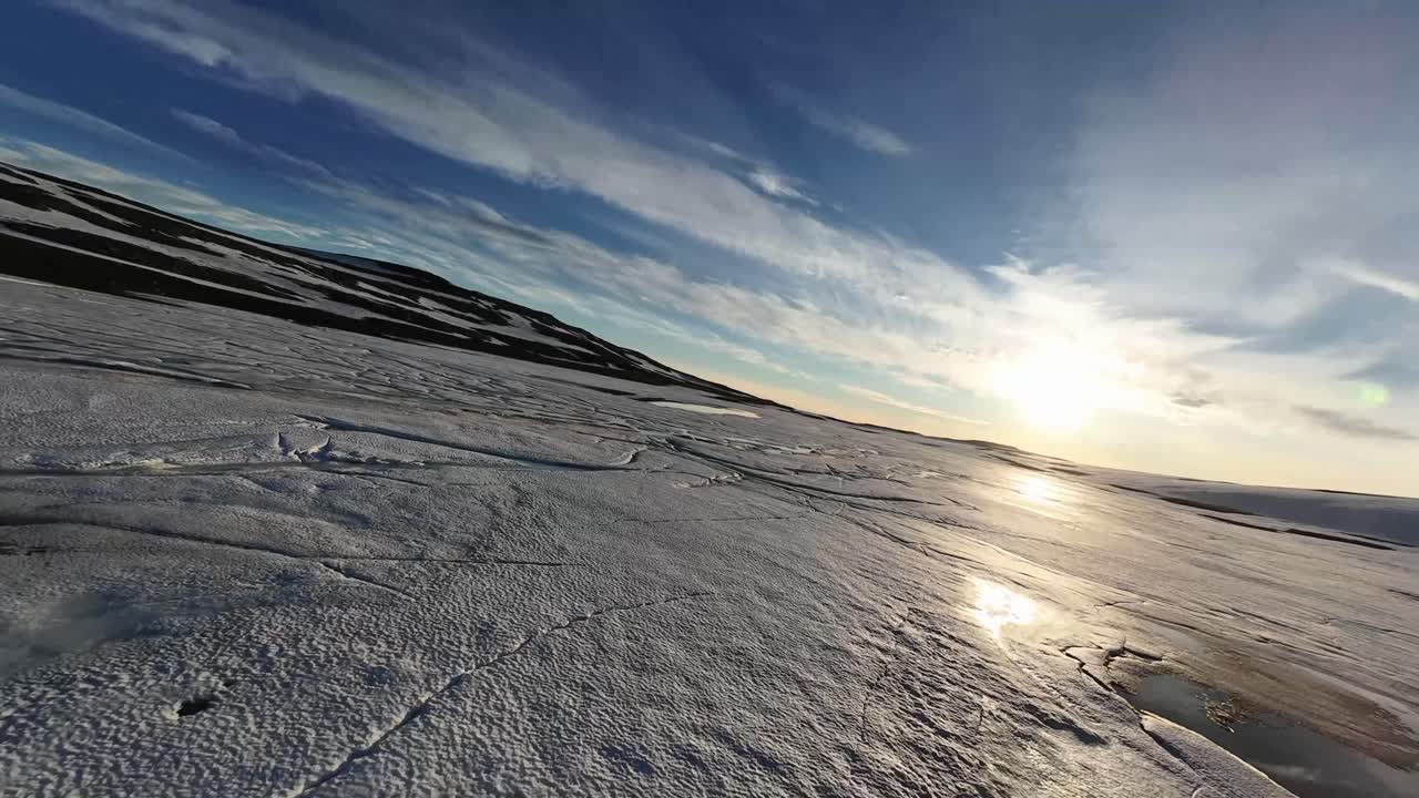 Un drone FPV a bassa quota sorvola un lago ghiacciato, che sembra un iceberg in Islanda, sfrecciando su ghiaccio testurizzato e crepe sotto drammatici cieli invernali, catturando velocità, isolamento e la cruda bellezza artica.