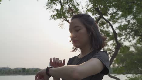 asian athlete woman using sport smart watch green nature park in evening sunset. female in sportswear touching screen application tracking activity and music. enjoy personal record data performance.