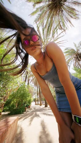 young woman in sunglasses with blowing hair among palm trees