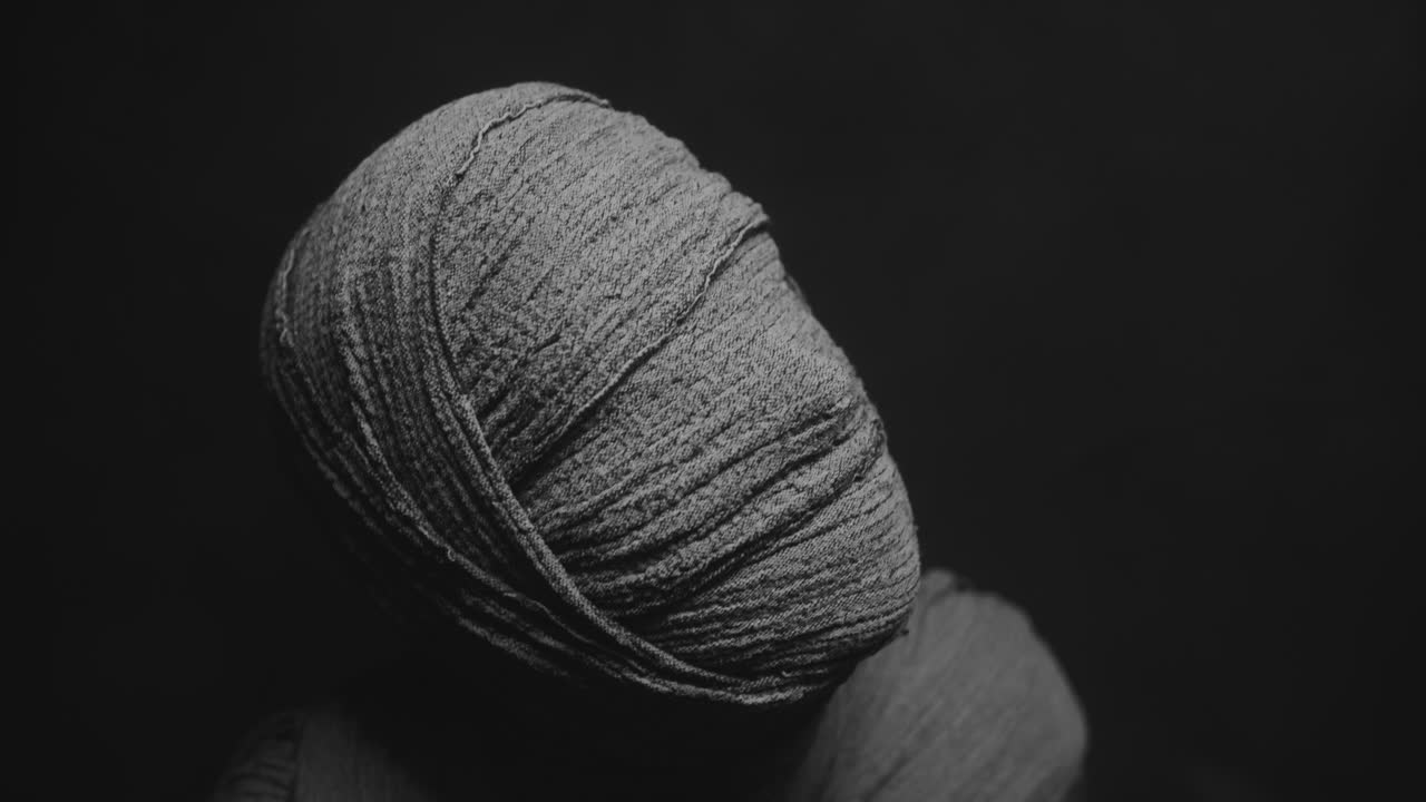 A mummy of a woman on a dark backdrop rises her head