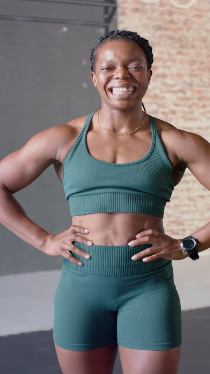 Video verticale: Donna sorridente in palestra, in abbigliamento da fitness, in piedi con sicurezza con le mani sui fianchi.