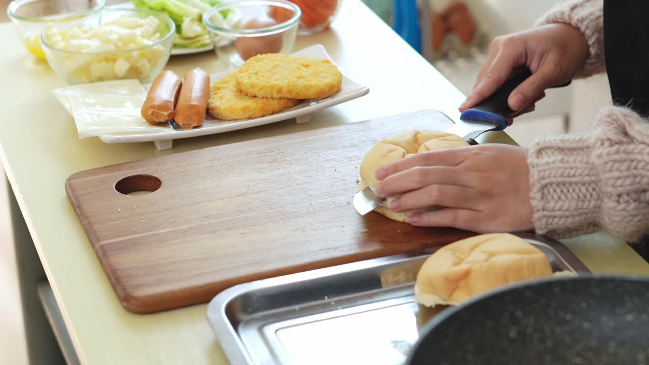 Giovane donna che taglia un panino in due parti per preparare un hamburger di pollo e formaggio.