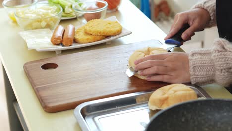 una mujer joven cortando un pan en dos partes para hacer una hamburguesa de pollo con queso
