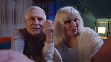 POV-of-cheerful-happy-Caucasian-senior-married-family-couple-talking-on-video-call-at-evening-home