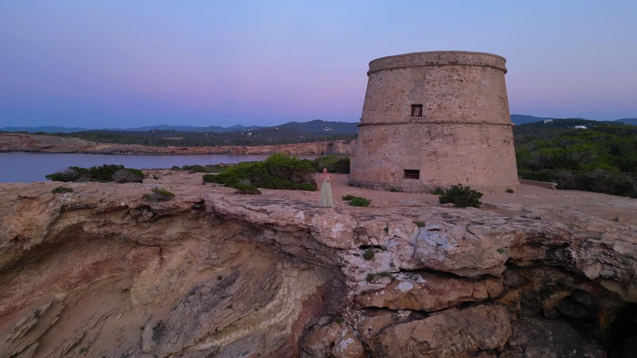 Barefoot hippie girl practicing yoga at sunset near Torre des Carregador, Ibiza, Spain. Perfect aerial view flight fly push forward drone