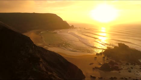 Volando-Cerca-A-Lo-Largo-De-Los-Acantilados-De-Las-Montañas-Oscuras-Girando-Tiro-Inclinado-Descripción-General-Sobre-La-Playa-De-Praia-De-Castelejo-Cabo-Sagres-Portugal,-Con-Rocas,-En-La-Impresionante-Puesta-De-Sol-Dorada-Con-Un-Estilo-Cinematográfico-épico