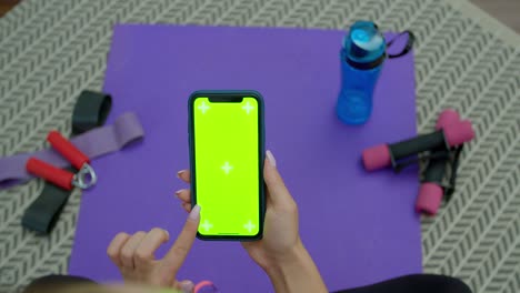 mujer de fitness usar teléfono inteligente con pantalla verde después de entrenar en casa. estilo de vida saludable. estiramiento, inclinarse hacia adelante. entrenamiento a distancia