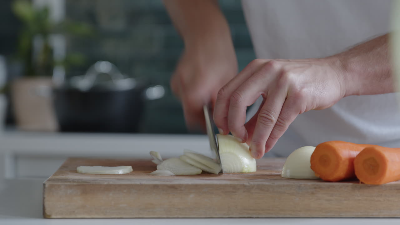 Close-up of man cutting fresh onions with a knife in a modern kitchen