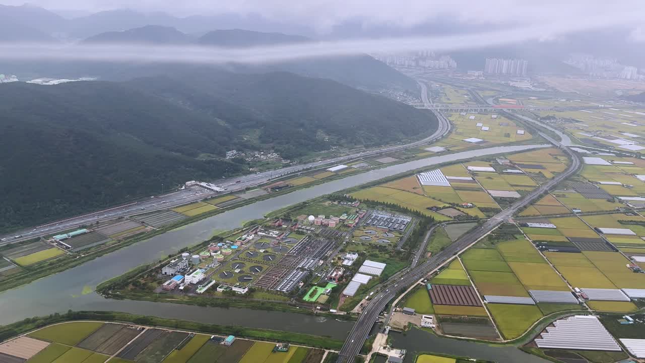 Foggy aerial view of farmland, a river, and a mountain near Busan in a tranquil, misty setting