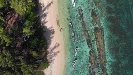 Toma-Aérea-De-4k-De-Arriba-Hacia-Abajo-De-Agua-Azul-Clara-A-Lo-Largo-De-La-Playa-Con-Botes-Blancos-Enfocados-Y-Simetría-Perfecta,-Pasamontañas,-Mauricio