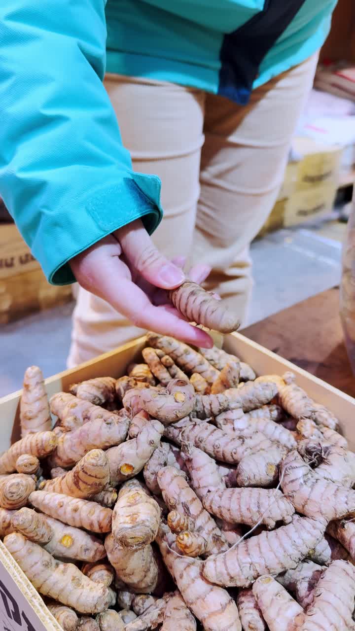 Donna che seleziona radice di curcuma fresca a una bancarella del mercato