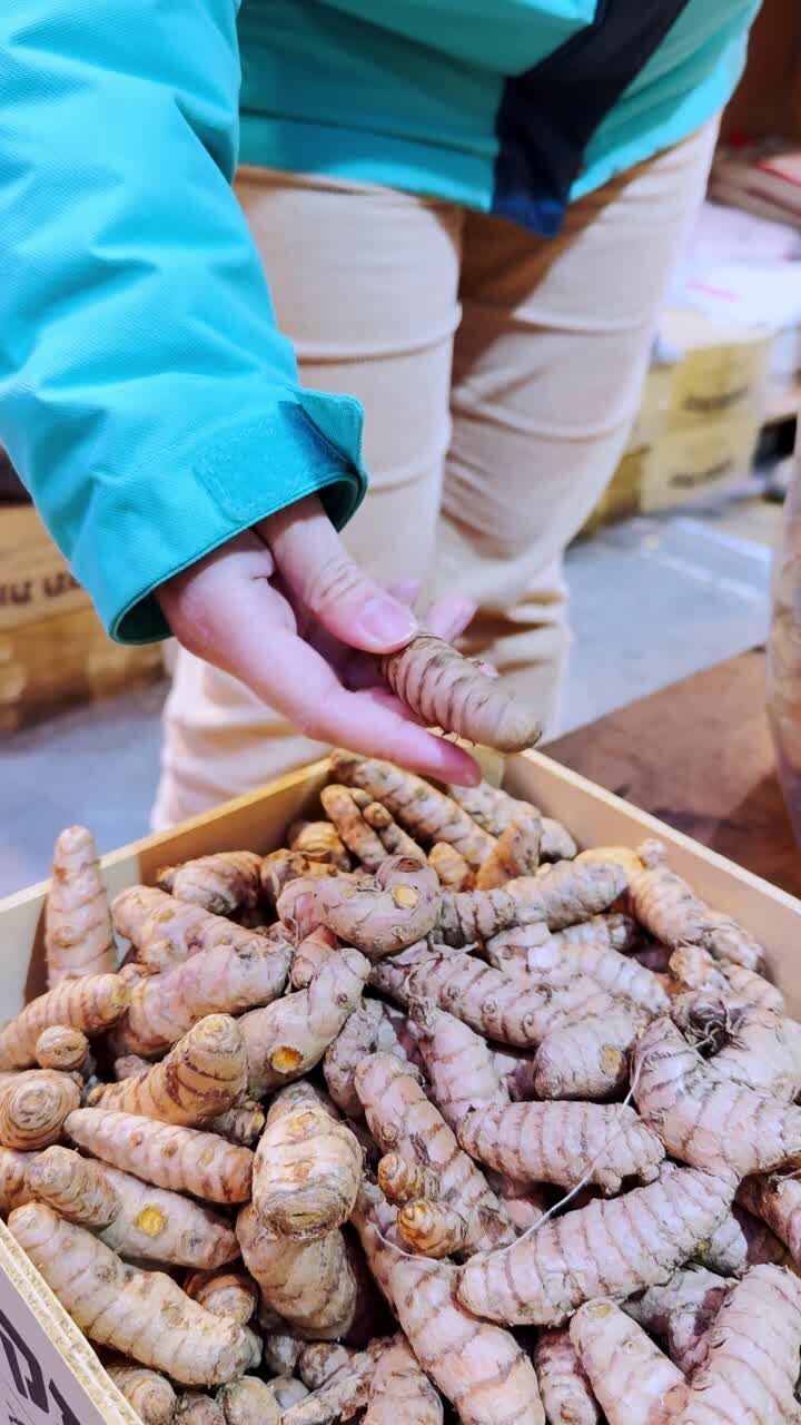 Woman selecting fresh turmeric root at market stall