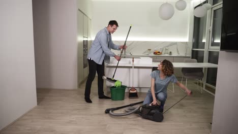 día de limpieza. pareja joven preparando herramientas para limpiar su apartamento - hombre tomando trapeadora, chica preparando aspiradora. van a limpiar la cocina del estudio juntos